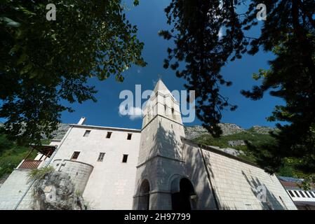 Blick auf den Glockenturm, aus weißen Steinblöcken, der in hellem Sonnenlicht an einem Sommernachmittag mit Bergen in Richtung blauen Himmel zeigt. Stockfoto