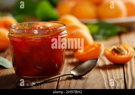Glas Glas Marillenmarmelade auf Holztisch mit reifen Aprikosen im Hintergrund Stockfoto