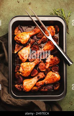 Gebackene Hähnchenschenkel, Drumsticks mit süßen Feigen und roten Zwiebeln in balsamischer Marinade auf Backblech, rostgrüner Hintergrund, Draufsicht Stockfoto