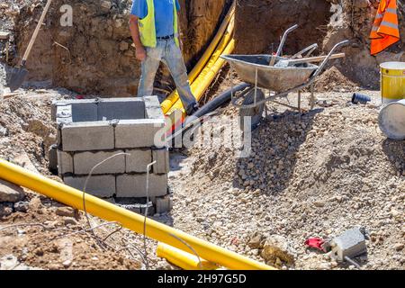 Bauarbeiter, die im Graben arbeiten und unterirdische Kommunikationsmittel für das neue Gebäude installieren. Stockfoto