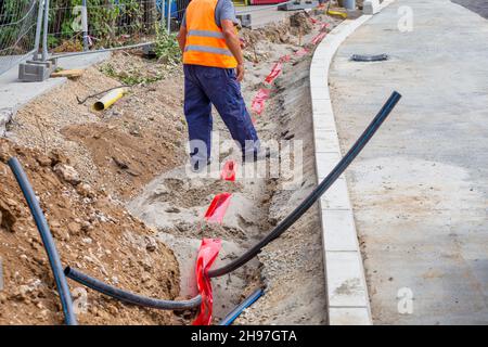 Arbeiter, der ein Warnband in den Graben legt, um einen Kabelkanal zu identifizieren. Stockfoto