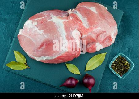 Ein großes Stück frisches blaues Fleisch auf einem Schieferstein und einem schwarzen Hintergrund mit Lorbeerblatt, Zwiebeln und Pfeffer. Draufsicht Stockfoto