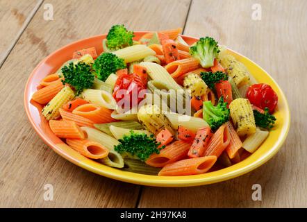 Pasta Penne mit Brokkoli, Karotten, Mais und Tomaten auf dem Holztisch Stockfoto