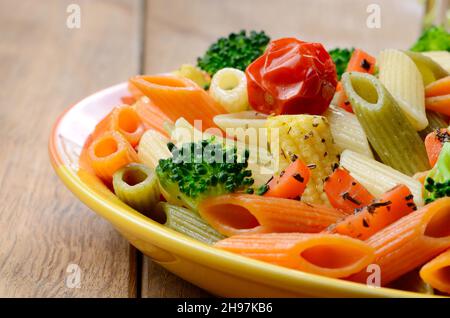 Penne Nudelsalat mit Brokkoli Karotte Mais und Tomaten auf dem Holztisch Stockfoto