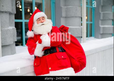 Der nachdenkliche weihnachtsmann lehnt sich im Winter an die Fassade eines Hauses Stockfoto