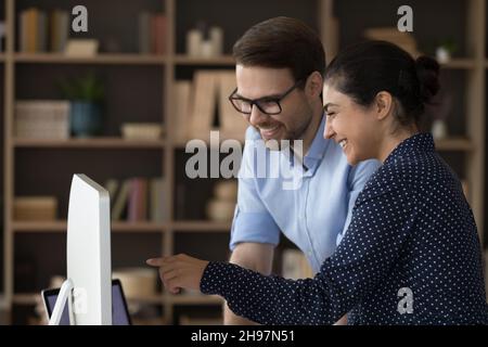 Zwei glückliche, vielfältige Mitarbeiter treffen sich am Computer und teilen den Monitor Stockfoto