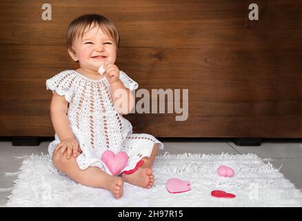 Baby mit Herzen auf einem hölzernen Hintergrund. Kind nagt weiße Kekse Stockfoto