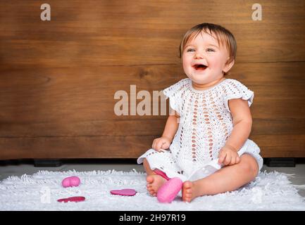 Baby mit Herzen auf einem hölzernen Hintergrund. Baby auf Teppich mit rosa Herzen lachend auf hölzernen Hintergrund Stockfoto