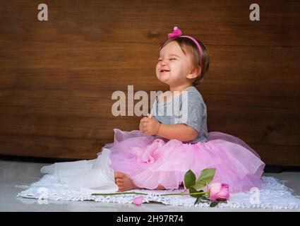 Baby im rosa Kleid auf dem Holzhintergrund. Kind mit einer Rose und einem Keks auf dem Holzhintergrund Stockfoto