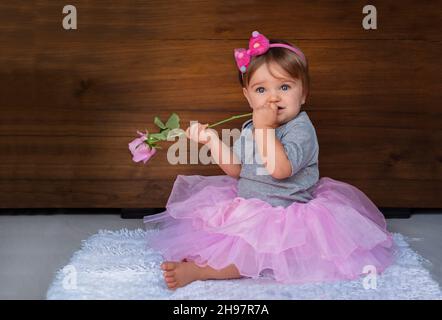 Porträt eines Kindes mit einer Rose auf einem hölzernen Hintergrund. Baby Mädchen in rosa Schmuck mit einer rosa Blume auf einem Holzhintergrund. Stockfoto