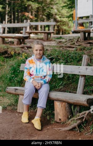 Nettes Teenager-Mädchen, das auf einer Holzbank im Park sitzt. Nettes Teenager-Mädchen, das auf einer Holzbank im Park sitzt. Stockfoto