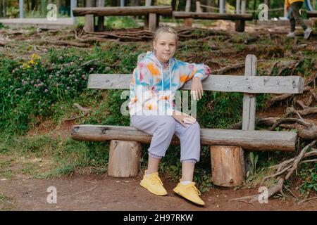 Nettes Teenager-Mädchen, das auf einer Holzbank im Park sitzt. Nettes Teenager-Mädchen, das auf einer Holzbank im Park sitzt. Stockfoto