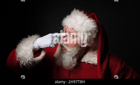 Lustiger Weihnachtsmann trägt rote Kostüm-Einstellbrille, während er auf schwarzem Hintergrund steht Stockfoto