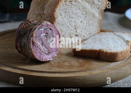 Geräuchertes Fleisch auf einem hölzernen Küchenbrett. Verschwommenes Brot und Hintergrund. Stockfoto