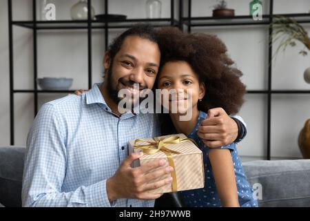 Fröhlicher afroamerikanischer Vater kuschelt kleine Tochter und feiert Geburtstag. Stockfoto