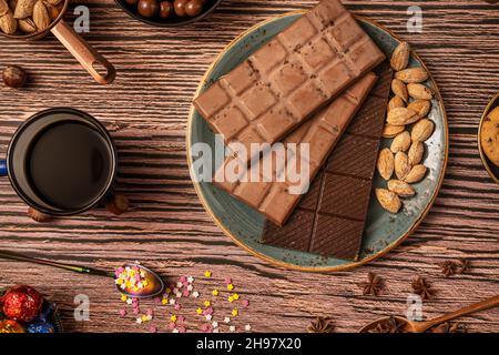 Stillleben mit Schokolade in Bars mit Kaffee und Tee, Schokolade, Haselnüssen und gerösteten gesalzenen Mandeln Stockfoto