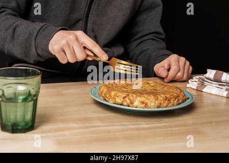 Die Hand eines jungen Mannes hält eine goldene Gabel, um ein frisch zubereitetes Kartoffelomelett zu essen Stockfoto