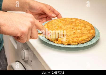 Gehacktes Kartoffelomelett mit goldener Abdeckung auf blauem Teller und weißer Küchentheke Stockfoto