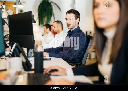 Junger Mann, der im Büro sitzt, am Computer schreibt, im modernen Büro Stockfoto