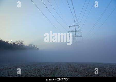 Großer Strommast (Strommasten) auch Freileitungsmast im Feld. Nebliger Wintermorgen. Vorderansicht. Stockfoto