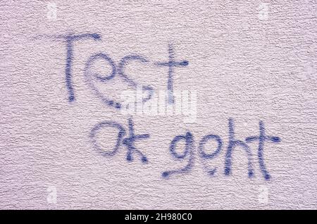 Graffiti mit dem deutschen Text 'Test ok geht' an einer Wand mit weißem Putz. Stockfoto