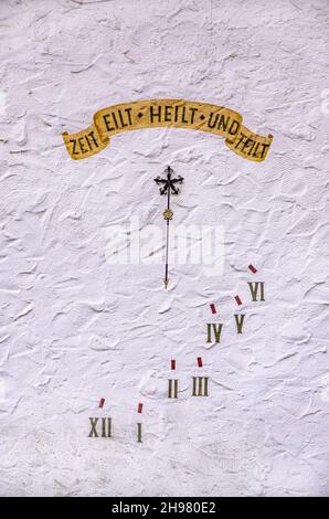 Sonnenuhr mit deutschem Motto Zeit EILT HEILT UND TEILT auf einer weißen Hauswand. Stockfoto