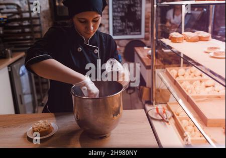 Die Köchin legt die Creme in einen Gebäckbeutel. Der Konditor gibt die Creme aus einem Mixer in einen Beutel. Stockfoto