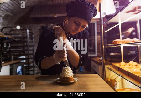 Ein Konditormädchen schmückt einen Shortbread-Kuchen mit einem Gebäckbeutel mit Proteincreme, drückt die Creme aus. Stockfoto