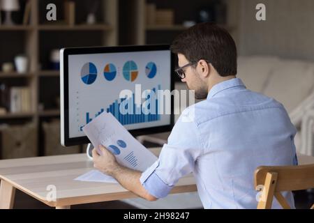 Fokussierter Millennial-Business-Mann, der Marketingberichte auf einem Desktop-Monitor analysiert Stockfoto