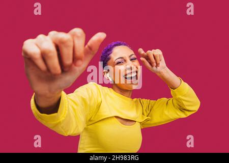 Junge Frau, die zu ihrem Lieblingslied tanzt. Fröhliche junge Frau, die fröhlich lächelt, während sie in einem Studio schnurlose Ohrhörer trägt. Frau mit lila Haaren s Stockfoto