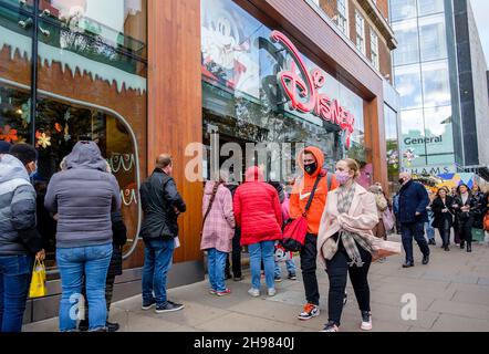 Weihnachtseinkäufer stehen Schlange, um den Disney-Laden in der Londoner Oxford Street zu betreten. Die britische Regierung hat Maßnahmen neu erlassen, die es zu einer rechtlichen Verpflichtung machen, Gesichtsbezüge in Geschäften und öffentlichen Verkehrsmitteln zu tragen, sofern sie nicht vom 30th. November ausgenommen sind, weil sie Bedenken wegen der Omicron-Variante von covid-19 hatte. Stockfoto