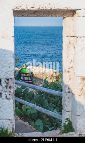 Mediterrane Meereslandschaft mit felsigen Klippen, wunderschönes blaues Meer, Vegetation, Steinmauern und Bücherregal mit Regalen aus altem Boot Stockfoto