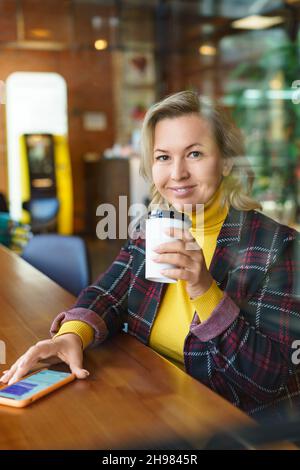 Eine wunderschöne kaukasische Frau mittleren Alters, die während einer Kaffeepause in einem Café in den sozialen Medien chattet. Stockfoto