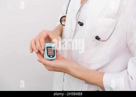 Pulsoximeter mit der Hand des Arztes auf Weiß isoliert. Messung der Sauerstoffsättigung, der Pulsfrequenz und des Sauerstoffgehalts. Das Konzept der tragbaren Digitaltechnik Stockfoto