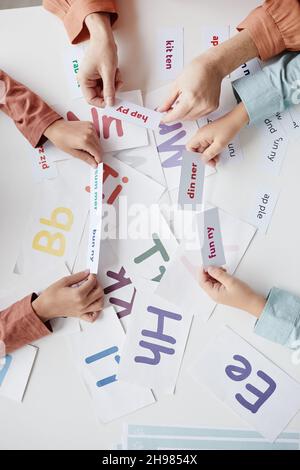 Nahaufnahme des Lehrers, der zusammen mit Schulkindern am Tisch spielt, Karten mit englischen Wörtern in der Hand hält und diese liest Stockfoto