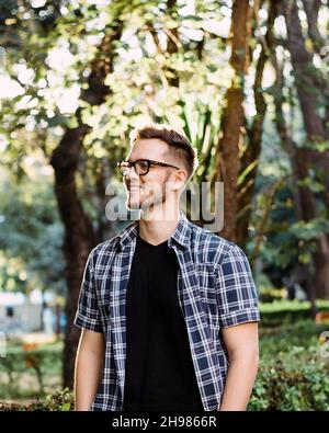 Ein Porträt eines selbstbewussten, fröhlichen jungen Mannes, der im Freien ein schwarzes T-Shirt mit kariertem Hemd trägt Stockfoto