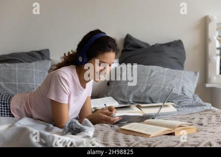 Lächelnde Frau mit Kopfhörern, die zu Hause online studiert und sich Notizen macht Stockfoto