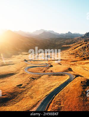 Malerische Luftaufnahme auf kurvenreicher Straße im herbstlichen Bergtal bei Sonnenuntergang. Das goldene Abendlicht beleuchtet die Berge und das orangefarbene Gras. Giau-Pass, Dolomiten, Dolomiten, Italien Stockfoto