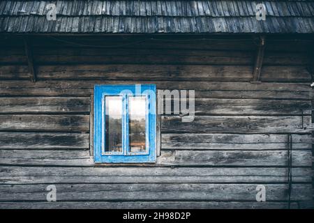Holzhauswand mit Holzdach und blauem Cyan-Fenster auf altes ukrainisches Haus Stockfoto