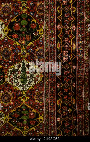 Ein Rand mit gemusterter Bordüre auf einem uralten persischen Teppich im „Ashan“-Stil mit schwarz-weißen Figurenzellen mit Blumenmustern auf einer burgun Stockfoto