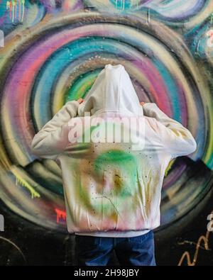 Eine Graffiti-Künstlerin posiert mit ihrer Kreation im berühmten Leake Street Tunnel in London. Stockfoto