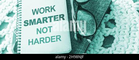 Stift, Brille und Spiralheft mit Work Smarter nicht härtere Wörter auf gehäkelter Stoffhintergrund. Karriere- und Geschäftskonzept Stockfoto