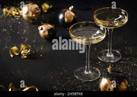 Festliche Neujahrsflöten und weihnachtliche Goldkugeln auf schwarzem Hintergrund. Nahaufnahme. Stockfoto