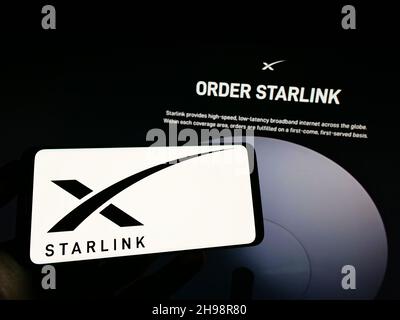 Person, die das Smartphone mit dem Logo der US-Satelliteninternet-Firma Starlink (SpaceX) auf dem Bildschirm vor der Website hält. Konzentrieren Sie sich auf die Telefonanzeige. Stockfoto