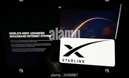 Person, die das Mobiltelefon mit dem Logo des US-Satelliten-Internet-Unternehmens Starlink (SpaceX) auf dem Bildschirm vor der Webseite hält. Konzentrieren Sie sich auf die Telefonanzeige. Stockfoto