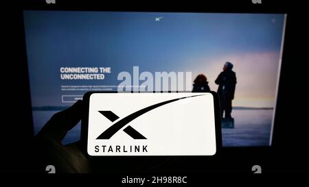 Person, die Mobiltelefon mit dem Logo der amerikanischen Satelliten-Internet-Firma Starlink (SpaceX) auf dem Bildschirm vor der Webseite hält. Konzentrieren Sie sich auf die Telefonanzeige. Stockfoto