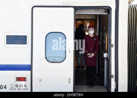 (211205) -- ZHANGYE, 5. Dezember 2021 (Xinhua) -- Eine Stewardess wird im Dienst in einem Hochgeschwindigkeitszug am Shandan Horse Ranch Bahnhof der Lanzhou-Xinjiang Eisenbahn im Bezirk Shandan, Stadt Zhangye, nordwestlich der chinesischen Provinz Gansu, 5. Dezember 2021 gesehen. Der Bahnhof Shandan Horse Ranch in über 3.000 Metern Höhe wurde am Sonntag in Betrieb genommen. Die Hochgeschwindigkeitszüge, die Passagiere nach Lanzhou, Xi'an, Urumqi, Jiayuguan und Dunhuang bringen können, werden jeden Tag in den Bahnhof fahren. Die Lanzhou-Xinjiang-Eisenbahn verbindet die nordwestliche Provinz Gansu und die Autonome Region Xinjiang Uygur. Stockfoto