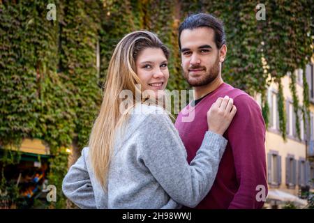 Junges Paar, das nach Rom reist. Schöne blonde Frau umarmt ihren Freund. Im Hintergrund eine Straße im historischen Zentrum mit einem efeubedeckten Gebäude Stockfoto