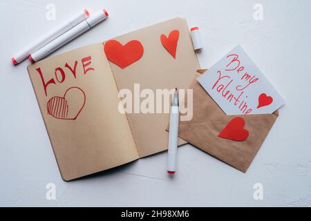 DIY valentine in einem Umschlag und eine Liebeserklärung in einem Skizzenbuch. Stockfoto