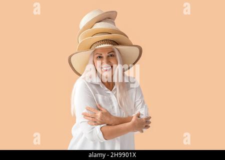 Schöne reife Frau trägt verschiedene Strohhüte auf farbigem Hintergrund Stockfoto